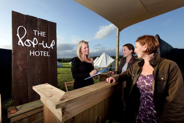 Receptionist and waitress Cary Mosley helps guests Brittany Roach and Kate Lewis check into the Pop-Up Hotel at the Glastonbury Festival(file photo) See SWNS story SWPOOL; Luxury at this yearís Glastonbury Festival will reach new heights with a extravagant pop-up hotel with its own SWIMMING POOL. Revellers who donít fancy staying in a cramped tent - and have up to £13k to spare - could find themselves a world away from the mud and sweat with a comfy alternative. After a long day on their feet, the glampers will be able to while away the evening with a relaxing soak in the exclusive pool before lounging on a secluded sun deck. And rather than curling up in a soggy, sweaty sleeping bag they will slip between the sheets of spacious queen-sized beds.